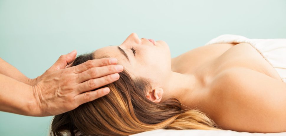 Profile view of a cute young woman getting her energy balanced at a reiki session in a health clinic and spa